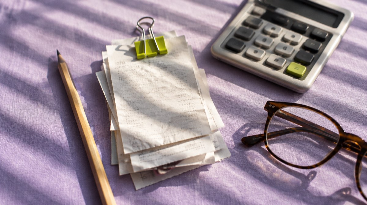 Scrivania notarile italiana con due documenti affiancati, uno con simbolo percentuale IVA e uno con timbro imposta di registro, modellino di casa sullo sfondo, tema finanziario professionale