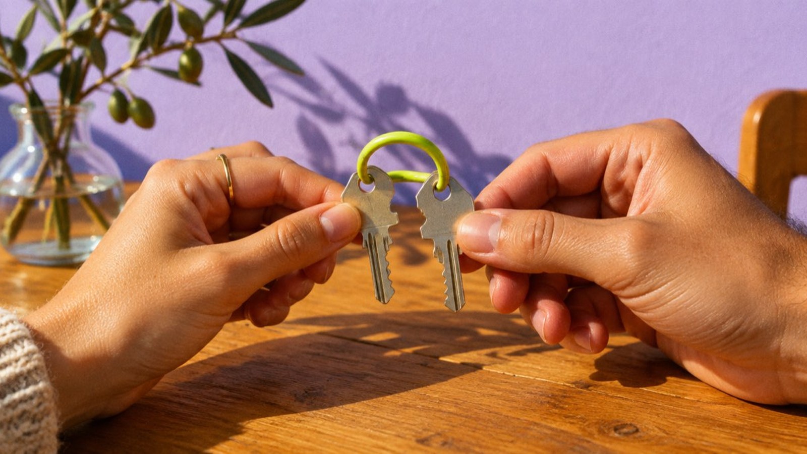 Due mani tengono due chiavi unite dallo stesso anello davanti a una parete lilla: la famiglia che chiede il mutuo insieme